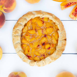 A flatlay image of an exquisite peach galette, filled with juicy yellow peaches, cradled in a golden pastry crust.