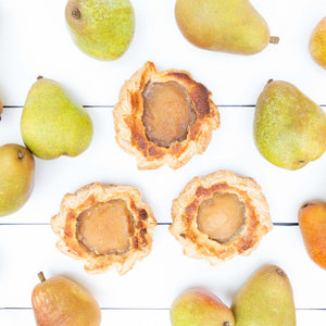 A flat lay featuring three delicious pear frangipane tartlets, cradled in golden pastry, surrounded by fresh juicy pears.
