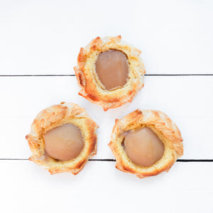 A flat lay featuring three handmade tartlets, filled with juicy pear slices, cradled within golden pastry.