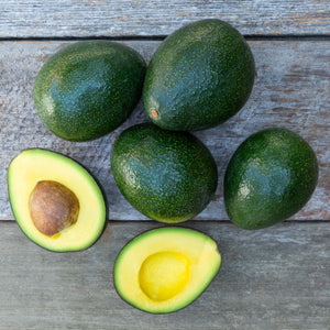 A close up image of vibrant, dark green avocados with buttery flesh, set against a rustic wooden background.